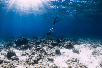 Woman freediver glides over coral bottom with fins in blue ocean.