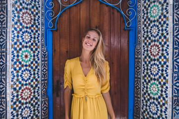 Half length portrait of happy female wanderer out sightseeing in foreign city during vacations overseas, positive woman traveler standing near bohemian mural building on unfamiliar street of Chaouen