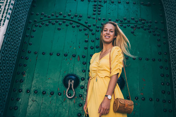 Half length portrait of positive hipster girl in trendy summer apparel posing near green ancient door in historic center of Morocco, cheerful carefree female laughing during sightseeing out