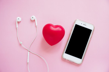 Red heart between the earphone and smartphone on pink background