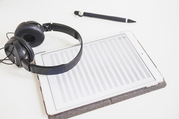 Headphone; stylus and graphic digital tablet with musical note on screen over white backdrop