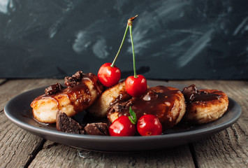 Gourmet breakfast - cottage cheese pancakes, cheese cakes, cottage cheese pancakes with cherries and chocolate in a brown plate. Useful dessert on a wooden table in rustic style. Selective focus.