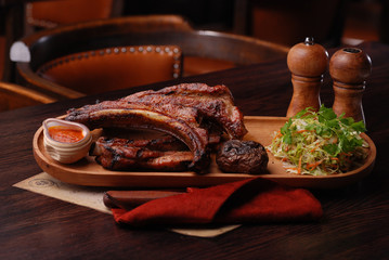 Baked ribs with suace and vagetables. Reastaurant dishes on the wooden table. Food photo for restaurant menu. Selective focus.