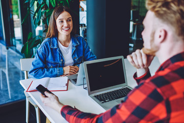 Positive male and female students enjoying live communication during break from e learning on modern laptops in campus, skilled successful freelancers collaborating on startup project via netbooks