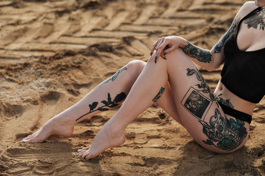Beautiful body of a woman covered with tattoos. Black underwear on the background of sand.