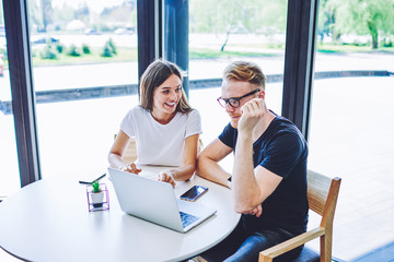 Positive male and female teenagers enjoying shopping togetherness in internet web store making payment online for some items using 4g wireless connection on modern laptop computer during leisure time