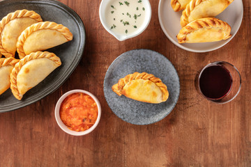 Empanadas with sauces and wine, shot from the top on a dark rustic wooden background with copyspace