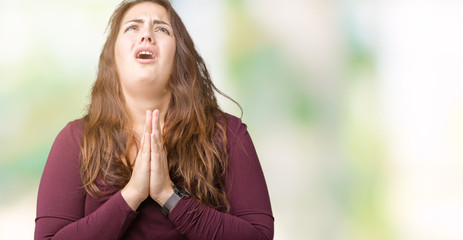 Beautiful and attractive plus size young woman wearing a dress over isolated background begging and praying with hands together with hope expression on face very emotional and worried. 