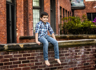 Fototapeta na wymiar Boy sitting on brick wall in jeans and plaid shirt
