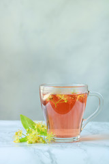 linden tea in a transparent cup with linden flowers on a gray background