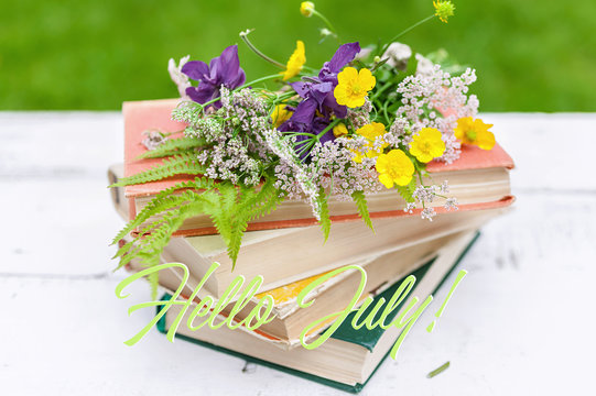Summer vintage composition. Old books, a bouquet of wild flowers on a rustic background. Caption: Hello July!