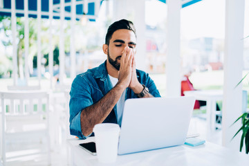 Contemplative young man watching tutorial webinar on modern laptop device connected to 4g wireless incafe terrace, pensive male software developer reading program code solving online problems