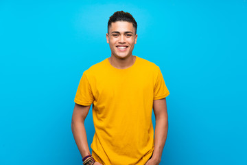 Young man with yellow shirt over isolated blue background laughing