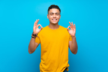 Young man with yellow shirt over isolated blue background in zen pose