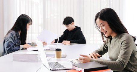 Asian women Students Smile and reading book and using notebook for helps to share ideas in the work and project. And also review the book before the exam