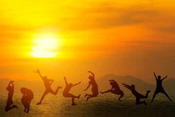 Fototapeta premium Young friends having fun on the beach and jumping against a sunset on summer.
