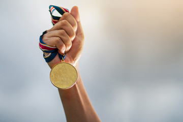 Hand holding gold medal on sky background - obrazy, fototapety, plakaty
