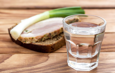 Glass of vodka with snack on the wooden table.