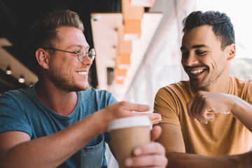 Excited Caucasian hipster guys feeling great during friendly meeting in cafeteria interior for...
