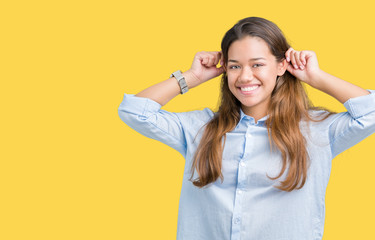 Young beautiful brunette business woman over isolated background Smiling pulling ears with fingers, funny gesture. Audition problem