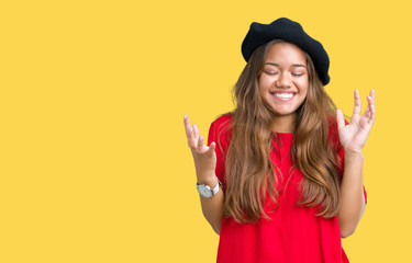 Young beautiful brunette fashion woman wearing red t-shirt and black beret over isolated background celebrating mad and crazy for success with arms raised and closed eyes screaming excited. 