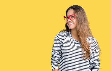 Fototapeta premium Young beautiful brunette woman wearing stripes sweater and red glasses over isolated background looking away to side with smile on face, natural expression. Laughing confident.