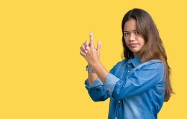 Young beautiful brunette woman wearing blue denim shirt over isolated background Holding symbolic gun with hand gesture, playing killing shooting weapons, angry face