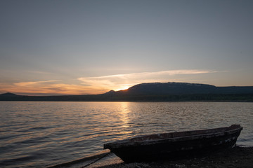 Old fishing boat on the lake at sunset tied with a chain. Old wooden boat on the shore