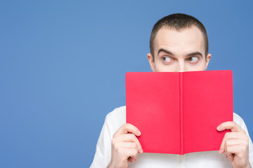 Student reads the book, looks out from behind a book, facial expressions, close up, background, copy space, for advertising