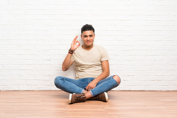 Young man sitting on the floor showing an ok sign with fingers