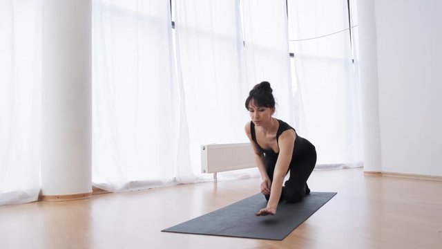 Front view of brunette coach sitting in half-twine pose doing pilates slow motion