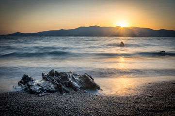Sunrise on Antiparos island, rock and beach in the foreground, Paros island in the background....