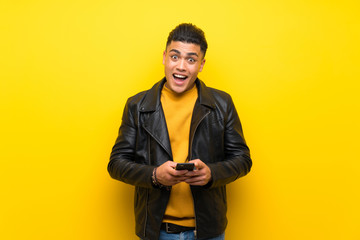 Fototapeta premium Young man over isolated yellow background surprised and sending a message