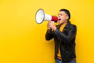 Young man over isolated yellow background shouting through a megaphone