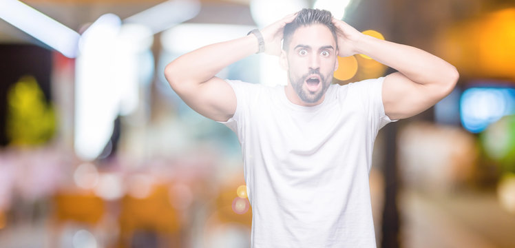 Handsome man wearing white t-shirt over night outdoors background Crazy and scared with hands on head, afraid and surprised of shock with open mouth