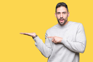 Young handsome man wearing sweatshirt over isolated background amazed and smiling to the camera while presenting with hand and pointing with finger.