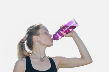 Young beautiful very pretty woman in a sporting suit drinks water from a bottle after workout in...
