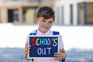 Happy little kid boy with backpack or satchel. Schoolkid on the way to school. Healthy adorable child outdoors With chalk desk for copyspace. Back to school or school's out.