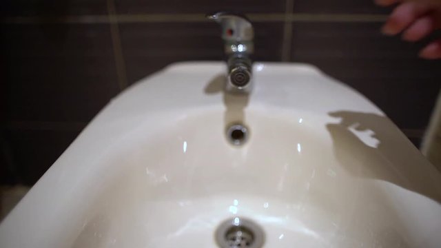 Closeup view of running water from tap of bidet in bathroom. 