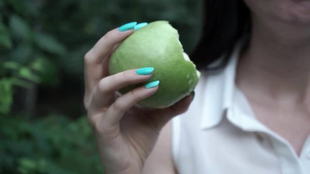 the girl chews the apple. in the foreground is a green apple. girl eating an apple and holding a fruit. big green apple.