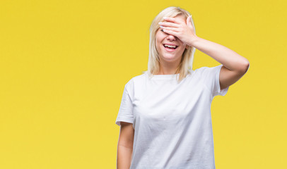 Young beautiful blonde woman wearing white t-shirt over isolated background smiling and laughing with hand on face covering eyes for surprise. Blind concept.