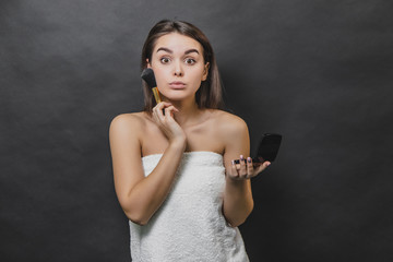 Obraz premium Surprised gorgeous girl with long hair posing, using makeup brush for applying blush.