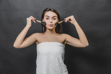 Obraz premium Beautiful young girl with two make up brushes in both hands. She is emitting kiss.