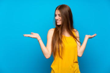 Young woman with long hair over isolated blue wall holding copyspace with two hands