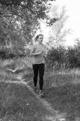 Athletic, beautiful girl jogging in the park or the forest and listening to music sunny summer morning, BW