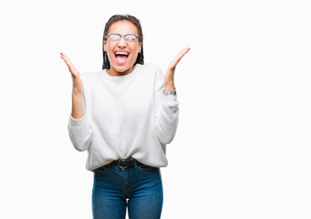 Young braided hair african american girl wearing glasses and sweater over isolated background celebrating mad and crazy for success with arms raised and closed eyes screaming excited. Winner concept