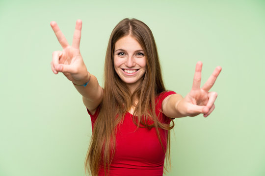 Young woman with long hair over isolated green wall smiling and showing victory sign