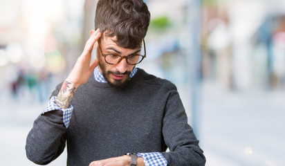 Young handsome smart man wearing glasses over isolated background Looking at the watch time...