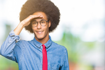 Young african american business man with afro hair wearing glasses and red tie very happy and smiling looking far away with hand over head. Searching concept.