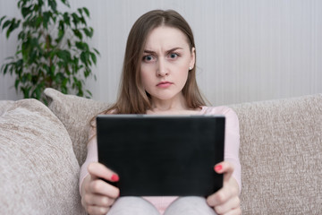 Evil woman watching video on tablet, sitting at home on the couch, toned